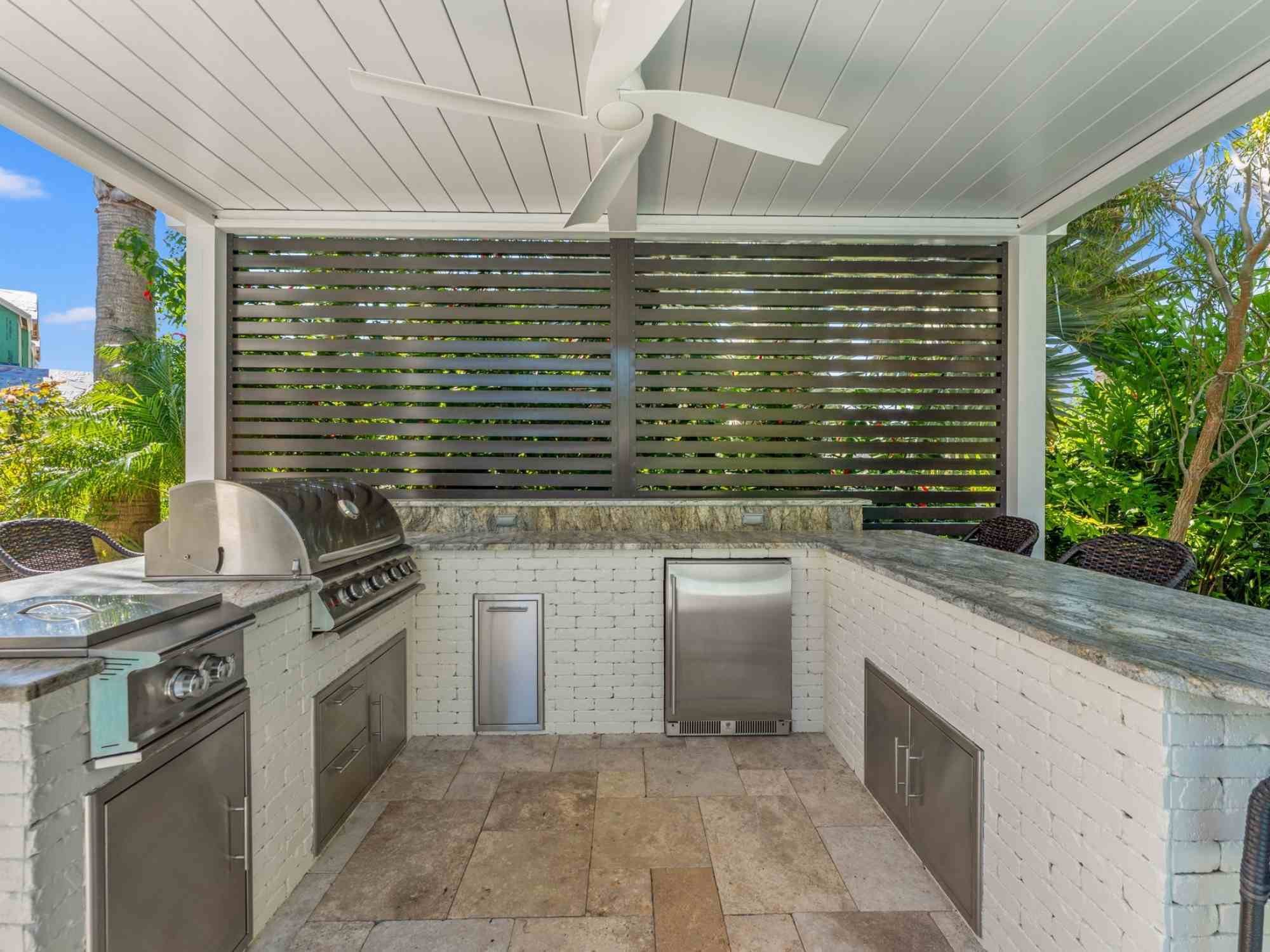 Image of the outdoor kitchen with built in grill, fridge, and motorized shades by Impact Enclosures