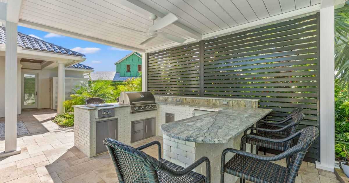 Image of an outdoor kitchen with a motorized screen and pergola by Impact Enclosures in Jacksonville, FL