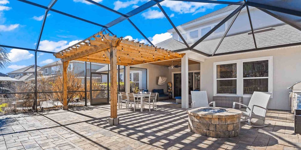 Image of an outdoor screen enclosure with wooden pergola and patio firepit by Impact Enclosures in Jacksonville, FL